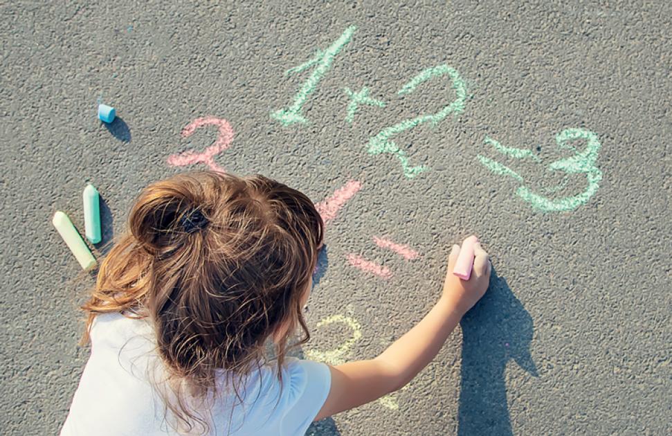 Fillette qui écrit des additions à la craie par terre